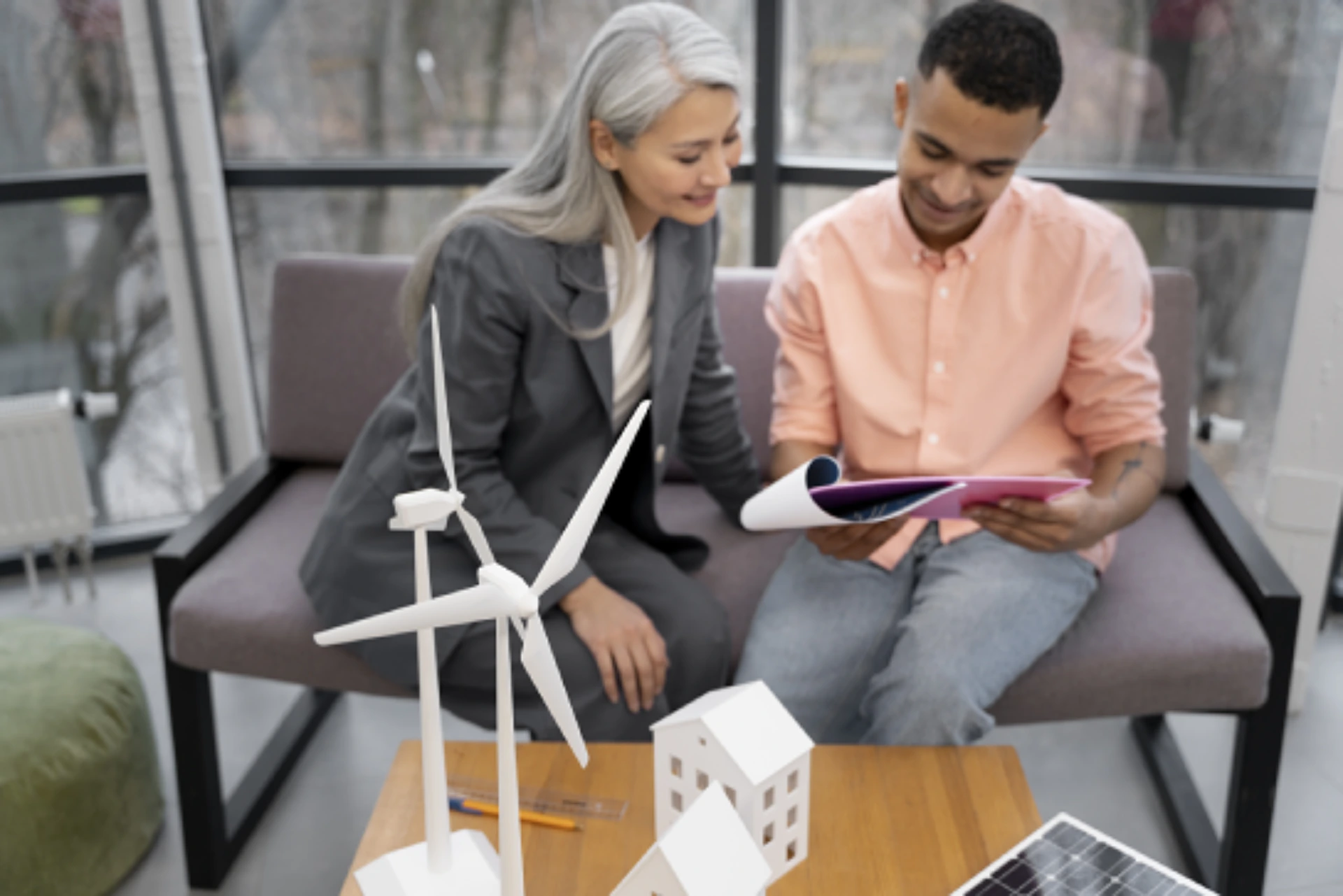 Zwei Personen unterhalten sich über die finanziellen Vorteile durch die KfW Förderung Photovoltaik und planen ihre nächsten Schritte. Im Vordergrund stehen zwei Modellwindräder auf einem Holztisch. 