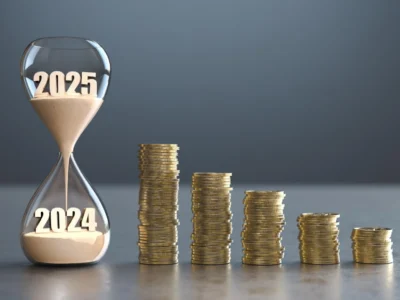 Eine Sanduhr, beschriftet mit 2024 und 2025, steht neben abnehmenden Stapeln von Münzen, was die zeitliche Entwicklung und potenzielle Veränderung der Einspeisevergütung 2025 symbolisiert.