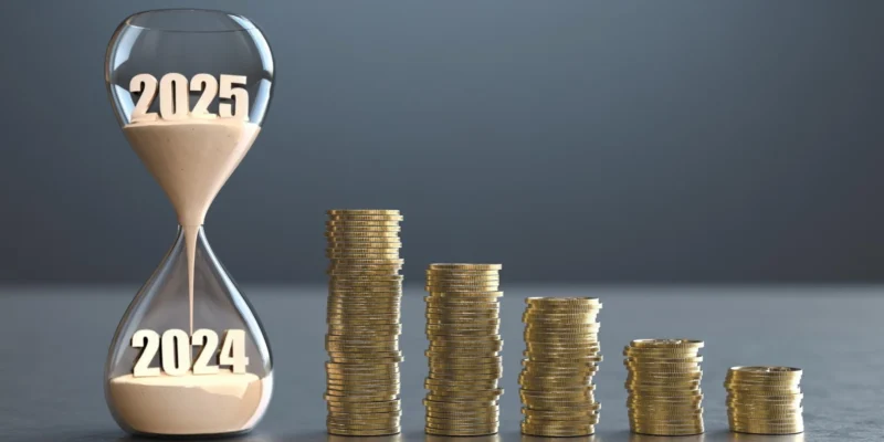 Eine Sanduhr, beschriftet mit 2024 und 2025, steht neben abnehmenden Stapeln von Münzen, was die zeitliche Entwicklung und potenzielle Veränderung der Einspeisevergütung 2025 symbolisiert.