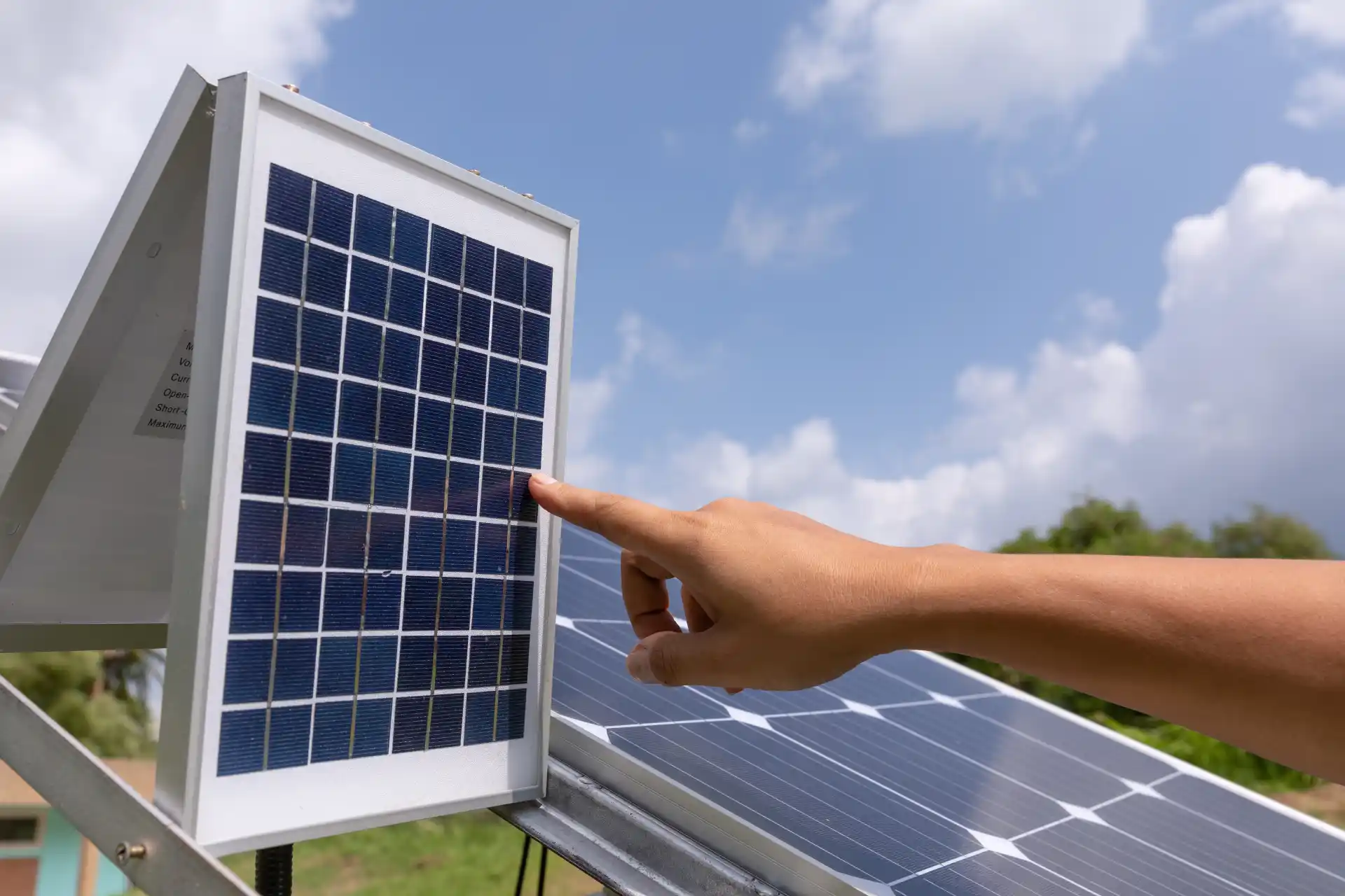 Nahaufnahme einer Hand, die die Oberfläche eines kleinen Solarpanels berührt, das zu einer Mini-Solaranlage gehört und draußen unter blauem Himmel steht.