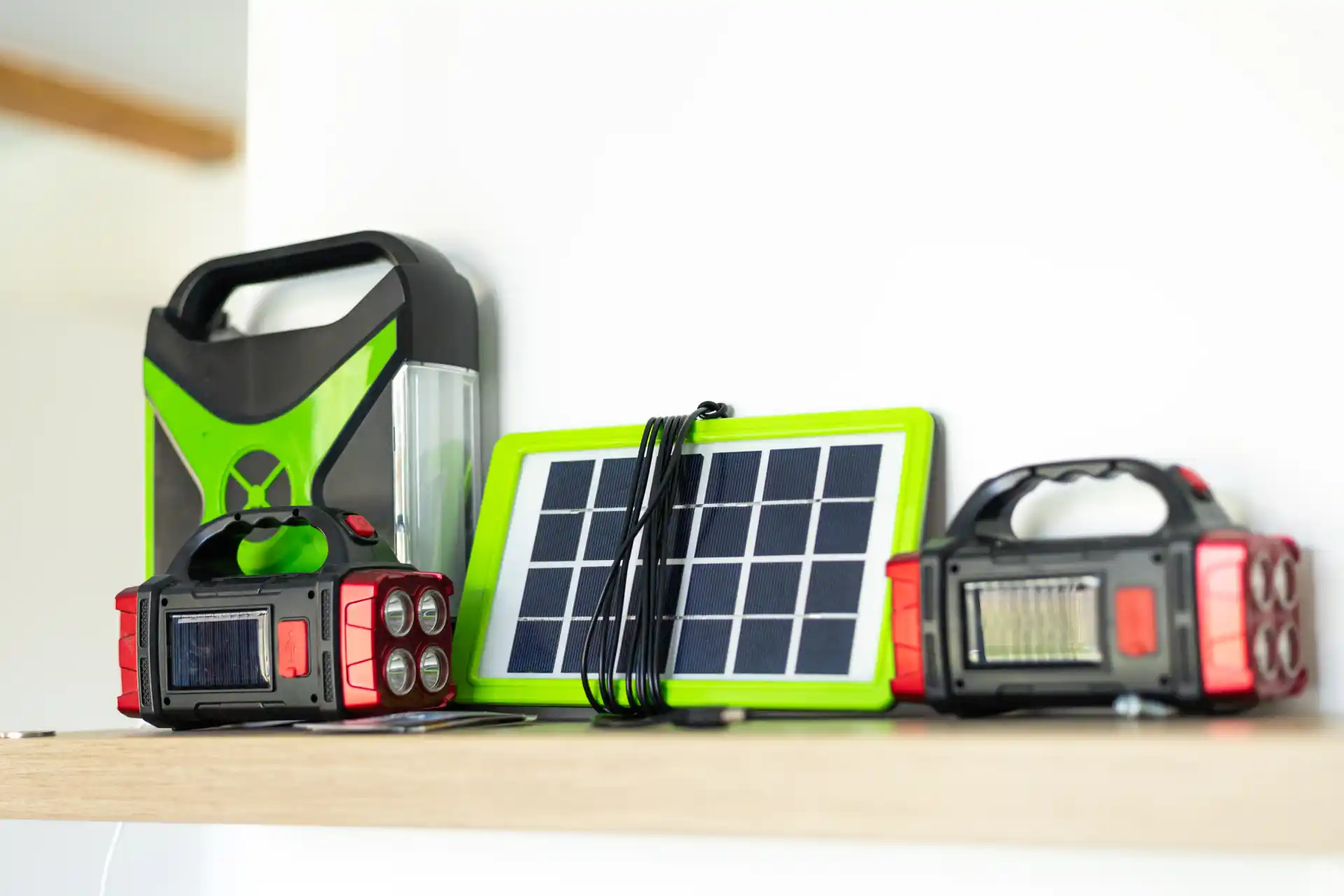 Kompakte Solarlampen und ein tragbares Solarpanel mit grünem Rahmen auf einem Regal im Innenraum, geeignet für Notfälle oder Camping.