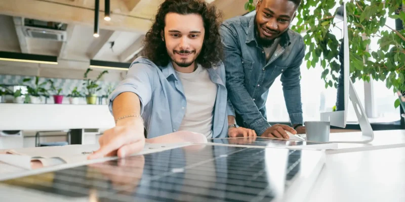 Zwei Männer betrachten ein Solarpanel, das auf dem Tisch vor ihnen liegt. Sie diskutieren über Möglichkeiten der Überschusseinspeisung.